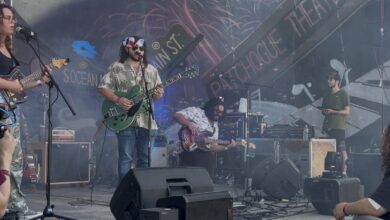 Three members of the band can be seen on a stage with a colofrul background during a performance